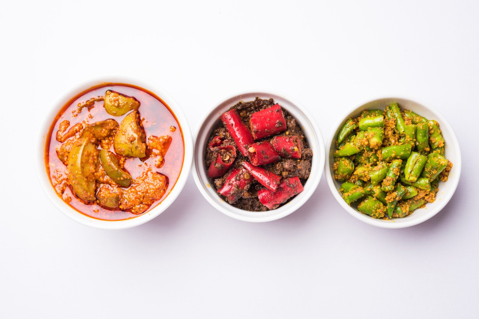 Three bowls filled with different colorful Pakistani pickles placed side by side.